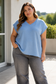 Woman wearing a blue top and gray pants standing outdoors.